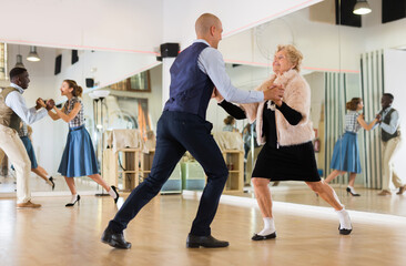 Man and elderly woman performing jazz dance in dancing room