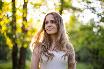 Beautiful young Russian girl dressed in a white dress, walks through the forest among the oaks in the rays of the sunset