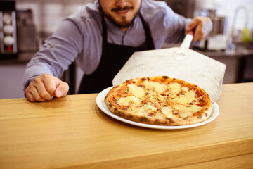 Partial shot of chef putting hawaiian pizza on plate in pizzeria 