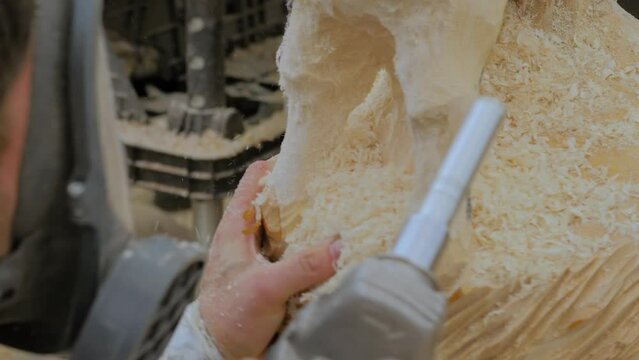 Man carpenter, wood sculptor using angle grinder with holes cutter saw attachment for carving wooden sculpture of goat with sawdust - close up. Carpentry, hobby, craftsmanship and woodworking concept
