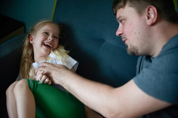 dad has fun playing with his child at home on the couch, tickling him