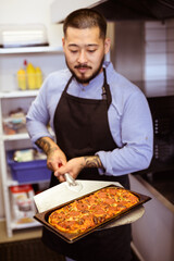 Blurred asian chef holding baked pizza with pepperoni in cafe 