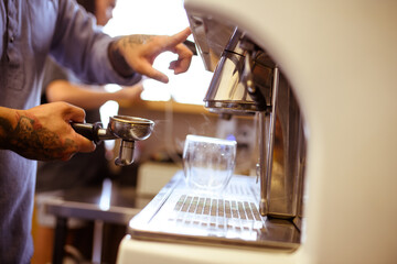 Partial view of tattooed barista holding holder near coffee machine in cafe