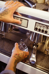 Partial view of tattooed barista holding glass near coffee machine in cafe