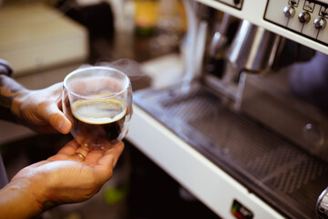 Faceless shot of barista holding glass of fresh coffee in cafe 