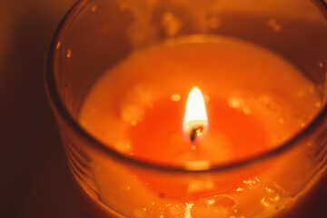 A pink or red wax scented candle in a glass container with a burning flame. Items to make the home...