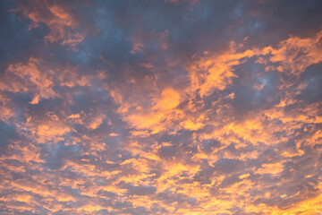 Bright orange rays of sunset sun illuminate clouds in blue evening sky

