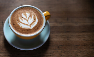 Morning coffee on a wooden table in a beautiful cup with a pattern on the foam. Aromatic coffee in a cafe at dawn.