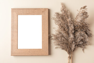 Blank photo frame with dry cane reeds or pampas grass on beige background. Flat lay. Mock up....