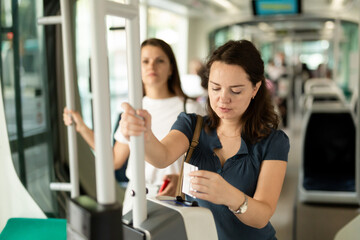 Young woman inserting ticket in modern punching machine, validating ticket in public transport..
