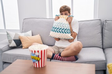 Young redhead man watching movie with scare expression at home