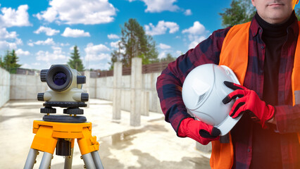 Surveyor equipment. Hard hat in builders hand. Optical level inside construction site. Man surveyor...
