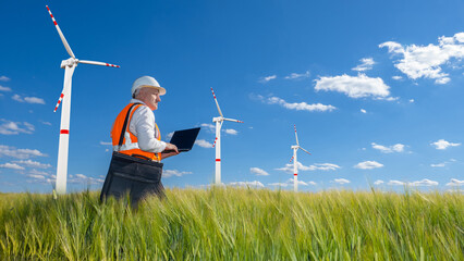 Man next to wind generators. Human with laptop in front power plant. Wind power plant in wheat...