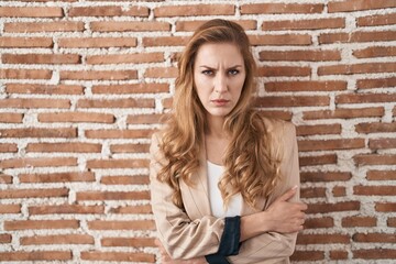 Beautiful blonde woman standing over bricks wall skeptic and nervous, disapproving expression on face with crossed arms. negative person.