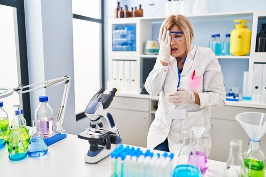 Middle age blonde woman working at scientist laboratory yawning tired covering half face, eye and mouth with hand. face hurts in pain.