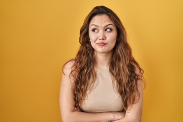 Naklejka premium Young hispanic woman standing over yellow background smiling looking to the side and staring away thinking.