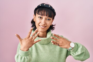 Young beautiful woman standing over pink background showing and pointing up with fingers number...