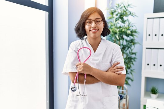 Young latin woman wearing doctor uniform standing with arms crossed gesture at clinic