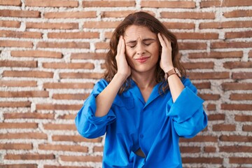 Beautiful brunette woman standing over bricks wall with hand on head, headache because stress. suffering migraine.