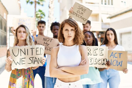 Young activist woman with arms crossed gesture standing with a group of protesters holding banner protesting at the city.