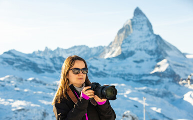 Interested woman photographer in sunglasses capturing scenic mountain views of Swiss Alps on sunny...