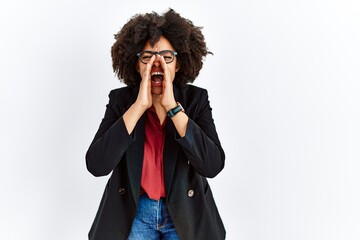 African american woman with afro hair wearing business jacket and glasses shouting angry out loud with hands over mouth