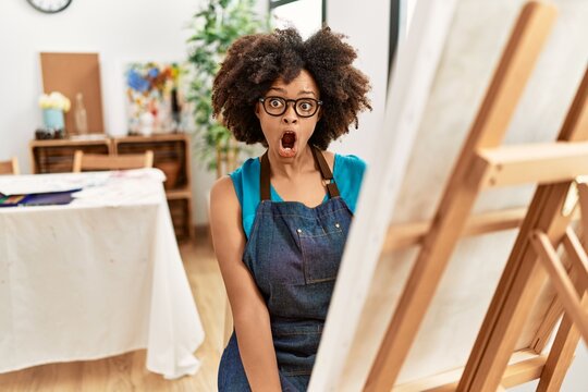 Beautiful african american woman with afro hair painting canvas at art studio scared and amazed with open mouth for surprise, disbelief face