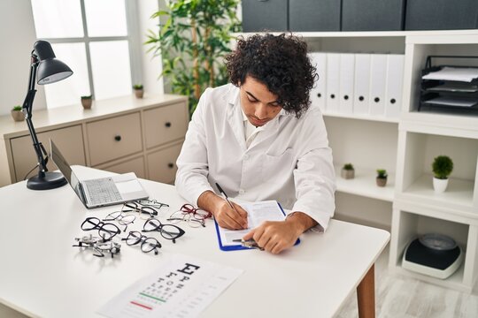 Young hispanic man optician writing on clipboard at clinic