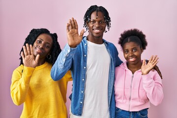 Group of three young black people standing together over pink background waiving saying hello happy and smiling, friendly welcome gesture © Krakenimages.com