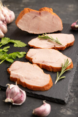 Smoked pork ham on cutting slate board on black concrete background. Side view, close up, selective focus.