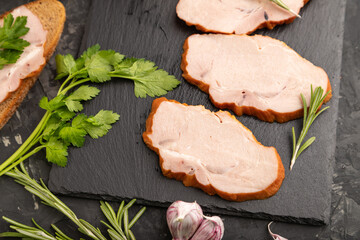 Smoked pork ham on cutting slate board on black concrete background. Side view, close up, selective focus.