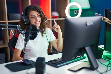 Hispanic woman with curly hair playing video games smiling happy pointing with hand and finger to the side