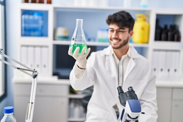 Young hispanic man scientist smiling confident measuring liquid at laboratory