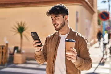 Young hispanic man using smartphone drinking coffee at street