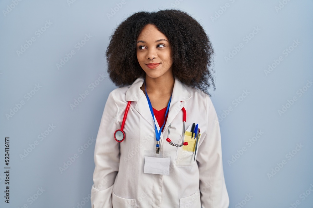 Sticker Young african american woman wearing doctor uniform and stethoscope smiling looking to the side and staring away thinking.