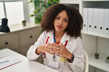 Young african american woman wearing doctor uniform looking to the camera at clinic