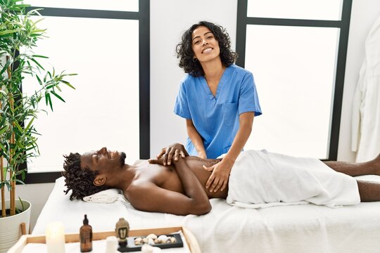 Young physiotherapist woman giving abdominal massage to african american man at the clinic.