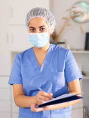Positive female doctor wearing face mask and blue overall meeting client before consultation