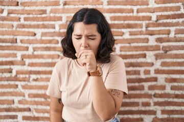 Young hispanic woman standing over bricks wall feeling unwell and coughing as symptom for cold or bronchitis. health care concept.