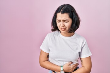 Fototapeta premium Young hispanic woman wearing casual white t shirt over pink background with hand on stomach because indigestion, painful illness feeling unwell. ache concept.
