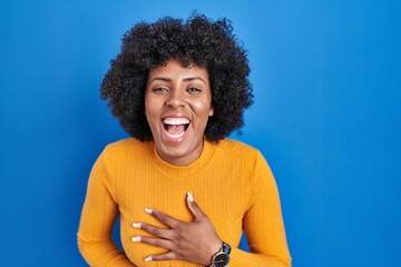 Fototapeta na wymiar Black woman with curly hair standing over blue background smiling and laughing hard out loud because funny crazy joke with hands on body.