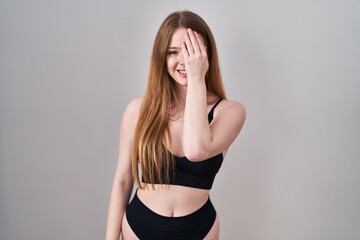 Young caucasian woman wearing lingerie covering one eye with hand, confident smile on face and surprise emotion.