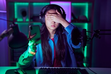 Young asian woman playing video games with smartphone covering eyes with hand, looking serious and...