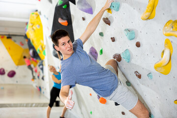 Young man showing thumb up while exercising on artificial climbing wall