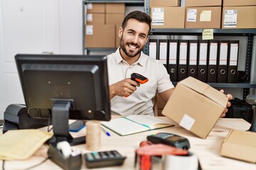 Young hispanic man smiling confident scanning package label with barcode reader at storehouse