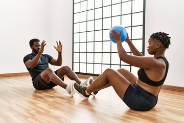 Fototapeta na wymiar Young african american sporty couple doing abs exercise using ball at sport center.