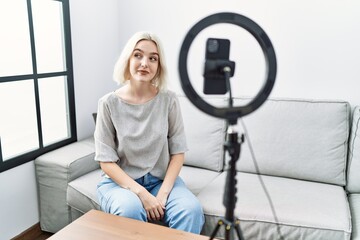Fototapeta na wymiar Young caucasian woman recording vlog tutorial with smartphone at home smiling looking to the side and staring away thinking.