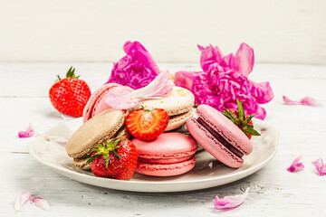 Macarons with strawberries and peonies flower petals, on a white wooden background