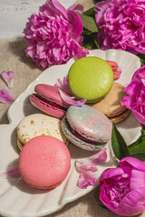 Macarons with a bouquet of peonies on white wooden background. Sweet dessert, pastel colors