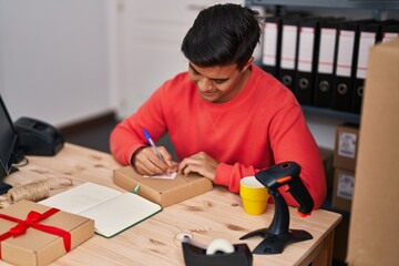 Young hispanic man ecommerce business worker writing on package at office